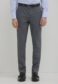 Pantaloni grigi aderenti realizzati in tessuto liscio, con frontale piatto e tasche. Abbinati a una cintura nera e scarpe nere lucide.