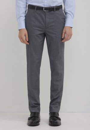 Pantaloni grigi aderenti realizzati in tessuto liscio, con frontale piatto e tasche. Abbinati a una cintura nera e scarpe nere lucide.
