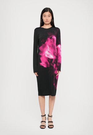 Vestido negro de manga larga con un vivo estampado floral en rosa. Tejido suave, corte a media longitud y silueta ajustada. La modelo lleva sandalias negras con tiras.