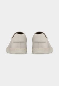 Ζευγάρι μπεζ αθλητικών παπουτσιών χαμηλού κορμού με χοντρές ελαστικές σόλες, φαίνεται από πίσω σε απλό λευκό φόντο.