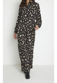 Czarny komplet w kwiatowy wzór składający się z koszuli z długim rękawem i kołnierzykiem oraz luźnych spodni z beżowymi i zielonymi akcentami.