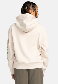 Felpa con cappuccio beige realizzata in morbido tessuto, con un vivace design floreale sulla manica sinistra e un orlo a coste.