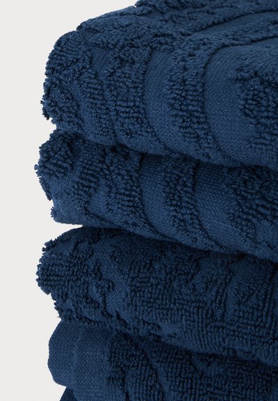 Pile de trois serviettes bleu foncé pliées avec des motifs géométriques et floraux texturés sur un fond blanc uni.