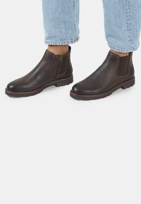 Stivaletti in pelle marrone con cerniere laterali, pannelli elastici e suola testurizzata. Presentano una forma snella e dettagli di cucitura a contrasto.