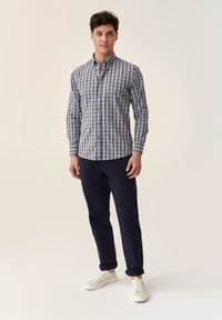 Een button-up shirt in een blauw-wit ruitpatroon, gemaakt van katoen, met lange mouwen, gecombineerd met marineblauwe broek en witte sneakers.