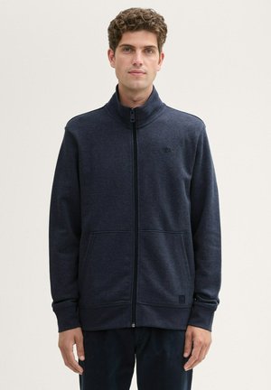 Felpa zip-up blu scuro con colletto alto, tasche frontali, texture morbida e logo discreto sul petto. Finitura in tessuto liscia.