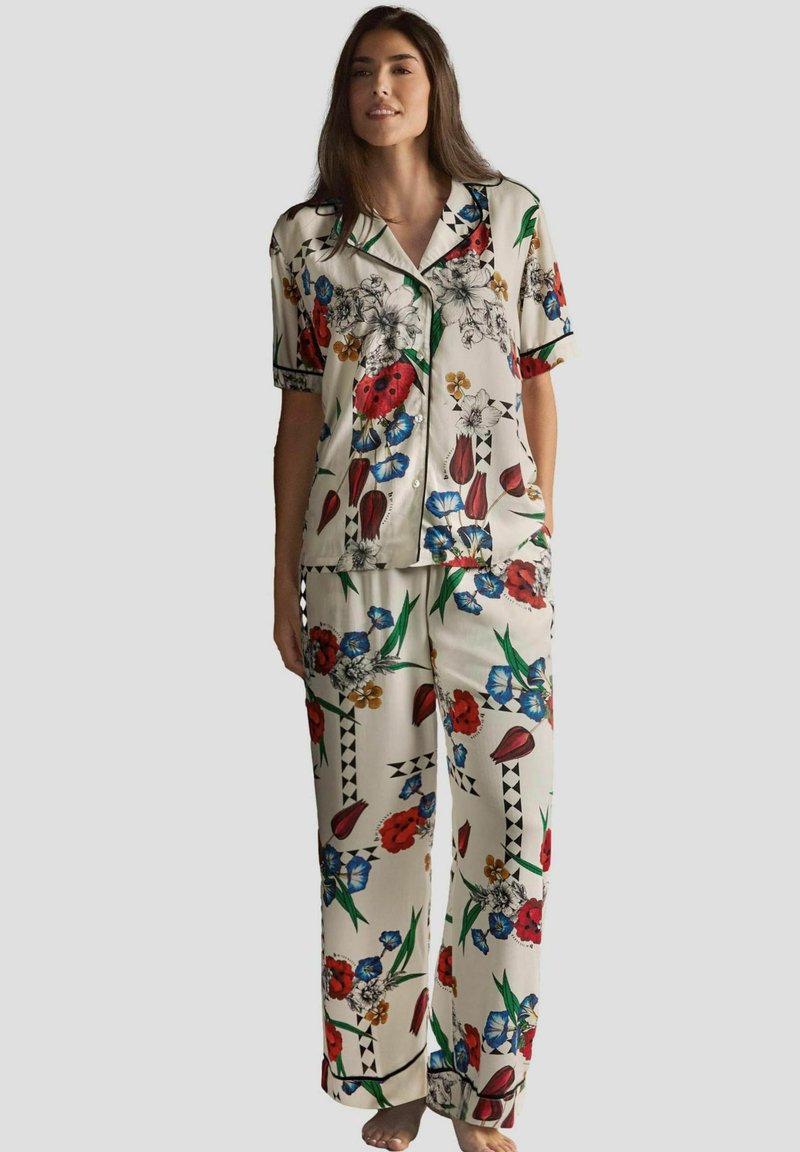 Set de pijama cu model floral în crem, cu accente roșii, albastre și verzi. Include mâneci scurte, guler și pantaloni largi cu o croială relaxată.