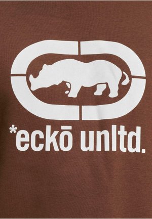 Ruda marškinėliai su dideliu baltu rinokero grafikų, esantį apibrėžtame stačiakampyje, ir užrašu "*eckō unltd." apačioje.