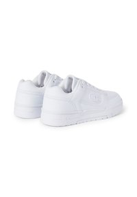 Zapatillas blancas de cuero con suela plana, cuello acolchado y un branding sutil en el costado. Diseño minimalista con una textura suave.