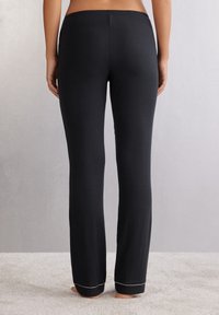 Zwarte katoenen blend broek met een rechte snit, elastische tailleband en contrasterende witte stiksels aan de zoom. Zachte textuur, ontspannen pasvorm.