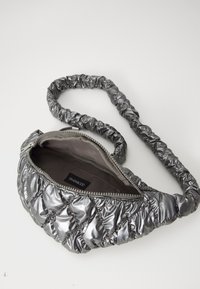 Borsa a tracolla grigia metallica trapuntata con tracolla arricciata e zipper, parzialmente aperta che mostra un interno in tessuto scuro con etichetta del marchio.