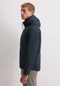 Granatowa kurtka z kapturem wykonana z lekkiego materiału o fakturowanym wykończeniu, wyposażona w zamek błyskawiczny i dwie przednie kieszenie.