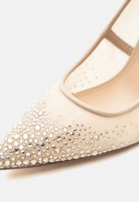 Κρεμ χρώματος μπαλαρίνα με μυτερή μύτη, καλυμμένη πυκνά με λαμπερά στρας στην περιοχή των δακτύλων, με λουράκι πίσω.