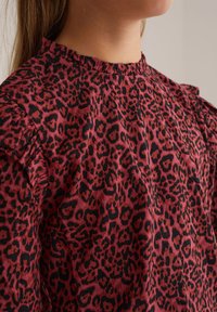 Raudona ir juoda leopardų rašto palaidinė su raukinėta apykakle ir pūstomis rankovėmis, pagaminta iš tekstūrinio audinio. Artimas vaizdas.