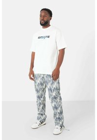 Witte T-shirt met grafische print, gecombineerd met textuur, blauw en wit gestreepte broek. Model draagt witte sneakers met zwarte accenten.
