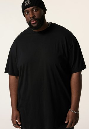 Camisa negra de gran tamaño con mangas cortas, hecha de algodón suave. Presenta un cuello redondo y un ajuste relajado, combinada con un gorro de punto negro.