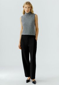 Gray sleeveless turtleneck top with a smooth texture, paired with high-waisted black trousers, and pointed black flats.
