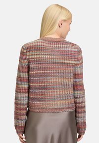 Woman wearing a multicolored striped knit sweater with long sleeves, viewed from the back, paired with a silky taupe skirt.