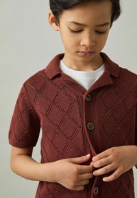 Cárdigan de punto de mangas cortas en color burdeos con un patrón de diamantes, que presenta un cuello, cierre de botones y una tela texturizada.