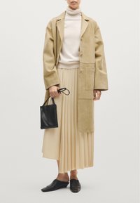 Tan ruskind lang frakke, creme turtleneck, plisseret beige nederdel, sort læder håndtaske og sorte spidse flade sko. Enkle og minimalistiske designelementer.