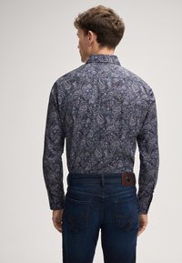 Langarmhemd in Dunkelblau mit einem komplizierten Paisleymuster; im Kontrast zu einer dunklen Jeans und hat ein Lederpatch am Bund.