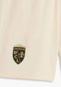 Beige sports trøje med struktureret stof. Har et fremtrædende sort og guld Racing Club de Lens-logo, der fremhæver 120 års eksistens.