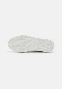 Semelle de chaussure en caoutchouc blanc avec une surface texturée présentant des motifs circulaires et des lettres de l'alphabet. Marquage distinctif "Calvin Klein" en relief.