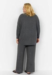 Grå loungewear-set bestående av en avslappnad långärmad topp och vida byxor, tillverkade av mjukt, texturerat tyg med ett subtilt mönster.