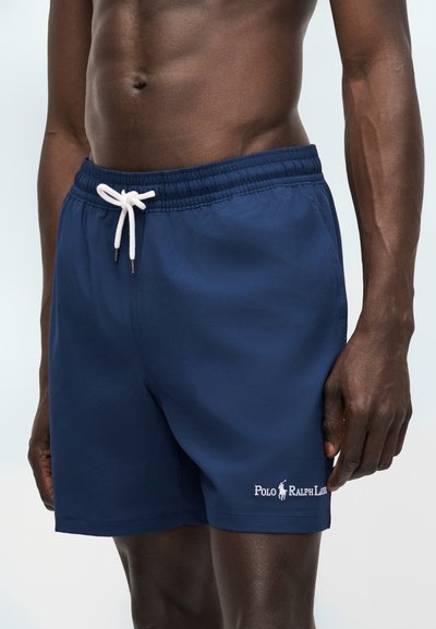 Αντρικός κορμός και ανώτερα πόδια που φορούν μπλε σκούρα μαγιό Polo Ralph Lauren με λευκό κορδόνι δεμένο στη μέση.