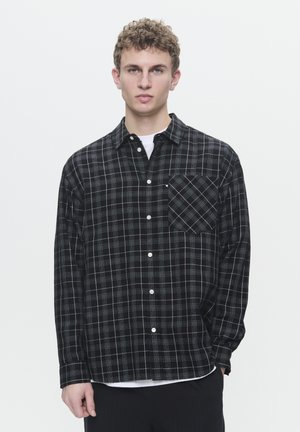 Black plaid button-up shirt featuring a pocket, white stitching, and a soft, textured fabric. Long sleeves with button cuffs.