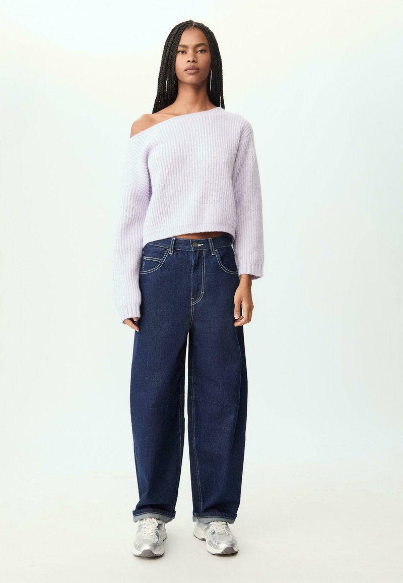 Lila ribbad stickad tröja med en axel ur design, kombinerad med mörkblå vida jeans och grå sneakers.