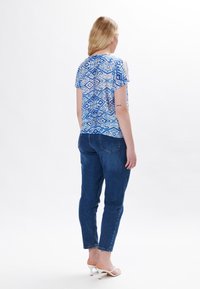 Top corto de manga corta con un patrón geométrico azul combinado con jeans azules. Tela suave, corte relajado y un sutil brillo en la parte superior.