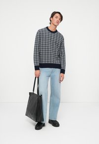 Ναυτικό και γκρι πλεκτό πουλόβερ με καρό σχέδιο, εφαρμοστό στη μέση. Ανοιχτό μπλε ίσια τζιν παντελόνια. Μαύρη δερμάτινη τσάντα ώμου με μακριές λαβές.