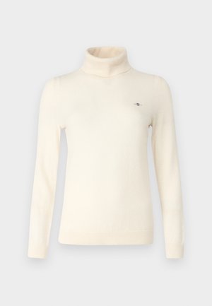 Suéter de cuello alto de color crema hecho de suave tejido de punto. Presenta mangas largas, un diseño ajustado y un pequeño detalle de logo en el pecho.