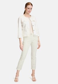 Biała dżinsowa kurtka z rękawami o długości trzy czwarte i ozdobnymi wycięciami na mankietach, zestawiona z jasnoszarymi spodniami do kostek.