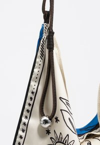 Torba płócienna z czarnymi kwiatowymi wzorami na kremowym tle, niebieski akcent wewnątrz, brązowy skórzany pasek oraz srebrne detale z kulkami.