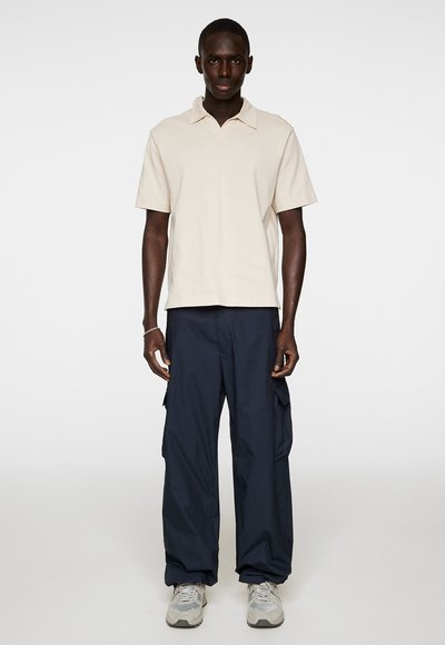 Hellbeige Poloshirt mit kurzen Ärmeln und Kragen, kombiniert mit locker sitzenden marineblauen Cargo-Hosen mit seitlichen Taschen und strukturiertem Stoff.