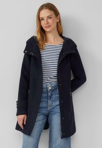 Marinefarbener Mantel mit Reißverschlussfront, Kapuze und Druckknöpfen; hat eine weiche Textur und zwei Seitentaschen; kombiniert mit einem gestreiften Hemd und Jeans.