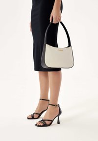 Borsa bianca e nera con manico arrotondato, caratterizzata da un accento del logo dorato. Indossata insieme a sandali neri con tacco alto e fasce.