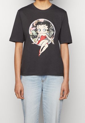 Person iført en sort T-shirt med stort grafik af tegneseriefiguren Betty Boop i rød kjole, siddende mod en farverig cirkulær baggrund.