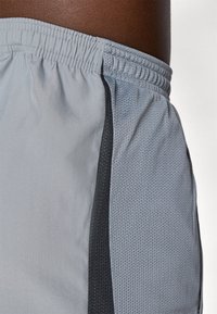 Shorts de sport gris avec un panneau latéral noir, fabriqués en tissu léger et respirant, doté d'une section en maille texturée pour la ventilation.