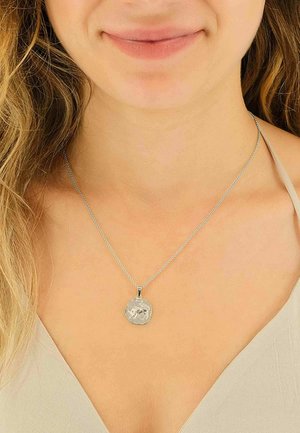 Collier en chaîne argentée avec un pendentif hexagonal texturé à surface polie, porté sur un cou de ton neutre.