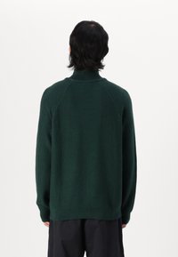 Dunkelgrüner Wollmischpullover mit hohem Kragen. Verfügt über Raglanärmel, eine weiche Textur sowie einen gerippten Bund und Ärmelabschlüsse.