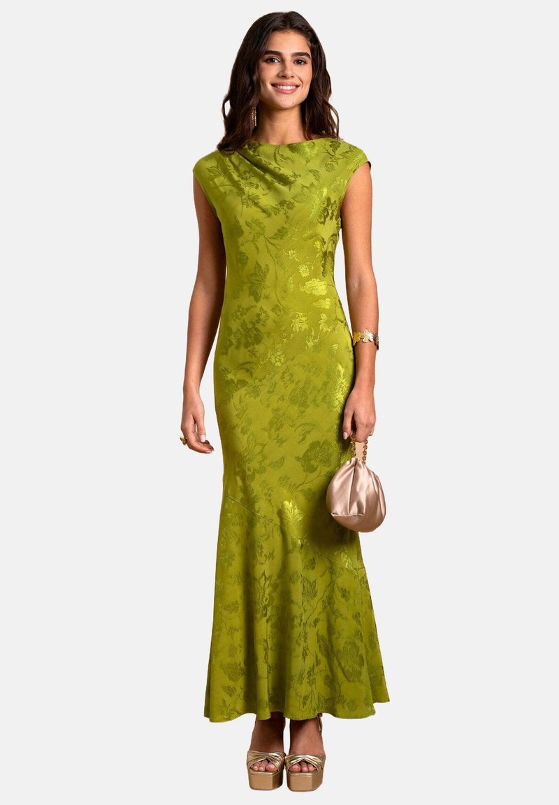 Grünes Abendkleid mit floralem Muster, tailliertem Oberteil, kurzen Ärmeln und ausgestelltem Saum. Kombiniert mit einer beigefarbenen Tasche und Plateauschuhen.