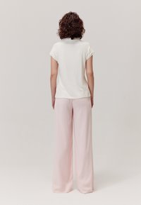 Biały, prążkowany top z krótkim rękawem w połączeniu z jasnoróżowymi spodniami o szerokich nogawkach, ukazującymi gładką tkaninę i luźny krój z widoku z tyłu.