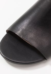 Černé kožené skluzavkové sandály s hladkým povrchem, otevřenou špičkou, širokým páskem a plochou podrážkou. Jednoduchá estetika bez viditelného kovového doplňku.