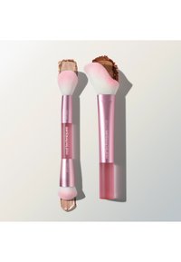 Twee make-upkwasten met roze handvat en witte en roze haren, elk brengt verschillende tinten bruine poeder aan op een wit oppervlak.