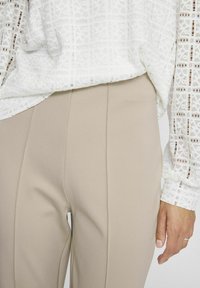 Blusa blanca de estampado con un corte holgado, combinada con pantalones beige de corte ajustado que presentan costuras verticales y una textura de tela suave.