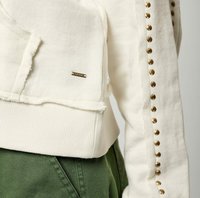 Sudadera blanca con textura acanalada, que presenta un detalle de hardware dorado y un bolsillo. Mangas adornadas con tachuelas doradas espaciadas uniformemente.