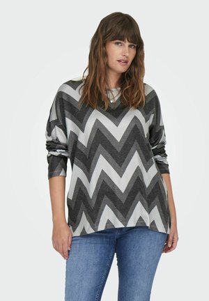 Grauer und weißer Sweatshirt mit Zickzackmuster, langen Ärmeln und lockerer Passform, aus weichem Stoff; kombiniert mit blauen Jeans.